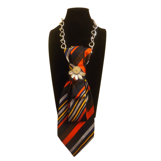 Colorful striped silk tie worn as a necklace with a gold sunburst pendant on a display bust