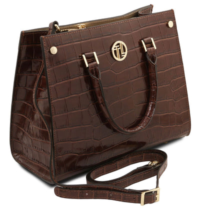 A dark brown crocodile-embossed leather handbag with gold-tone hardware, dual top handles, a top zipper, and a detachable shoulder strap, shown on a plain white background.