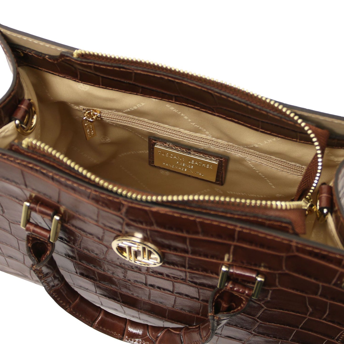 Close-up of the interior of a brown crocodile-embossed handbag with gold-tone hardware, a beige quilted lining, and a visible interior label reading TORY BURGER.