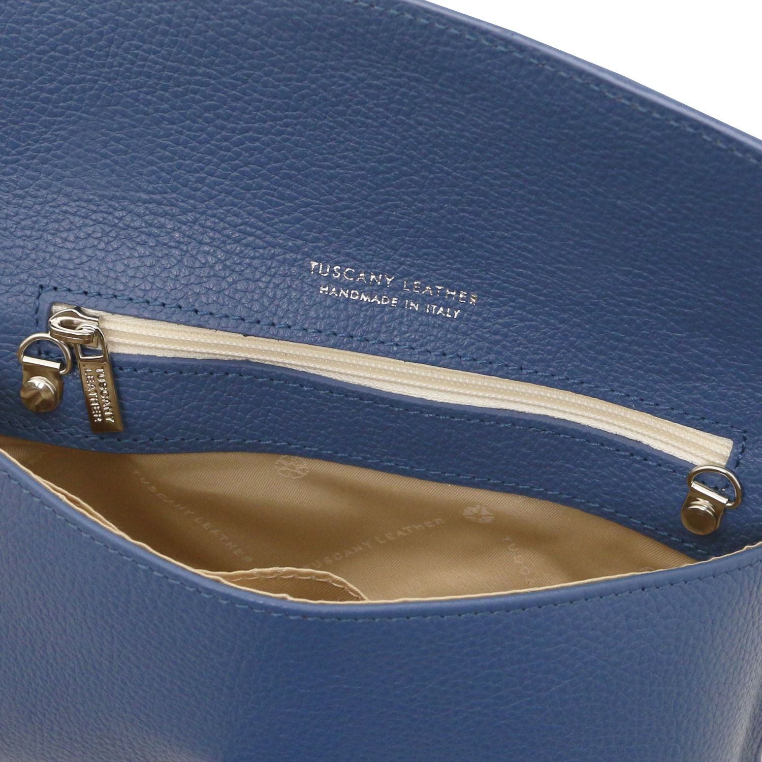 Close-up of blue leather clutch showing inner zip pocket with beige lining and gold zipper pull.