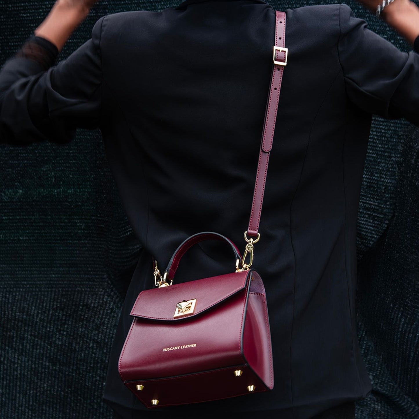burgundy leather TL Bag mini bag with gold hardware and a long strap worn over a black coat