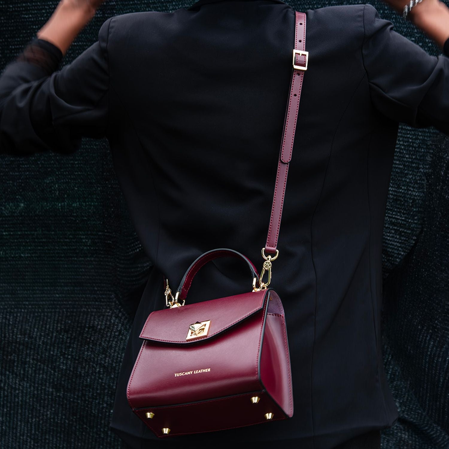 burgundy leather TL Bag mini bag with gold hardware and a long strap worn over a black coat