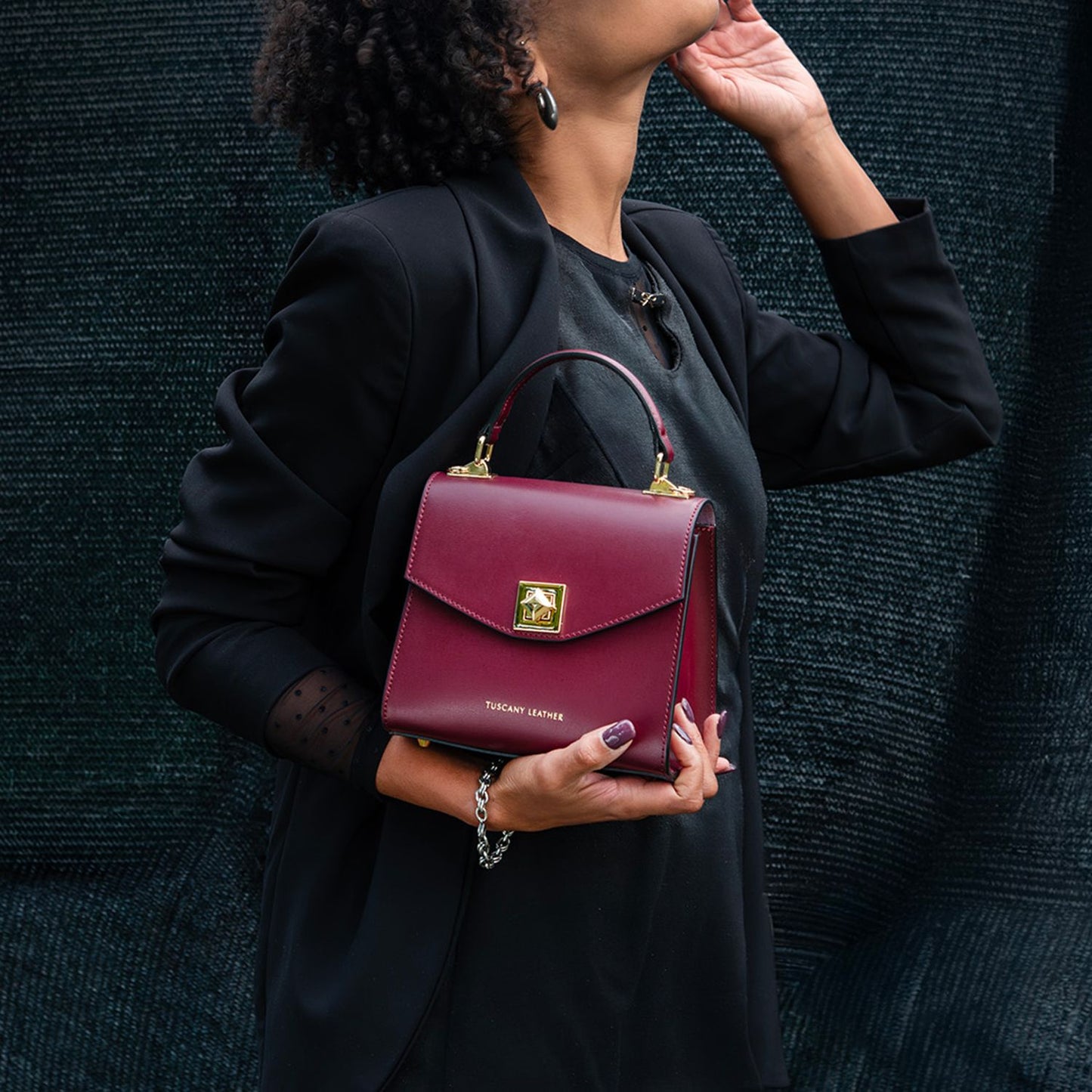 Burgundy leather TL Bag mini handbag with a gold square clasp and top handle, held by a person in a black blazer.