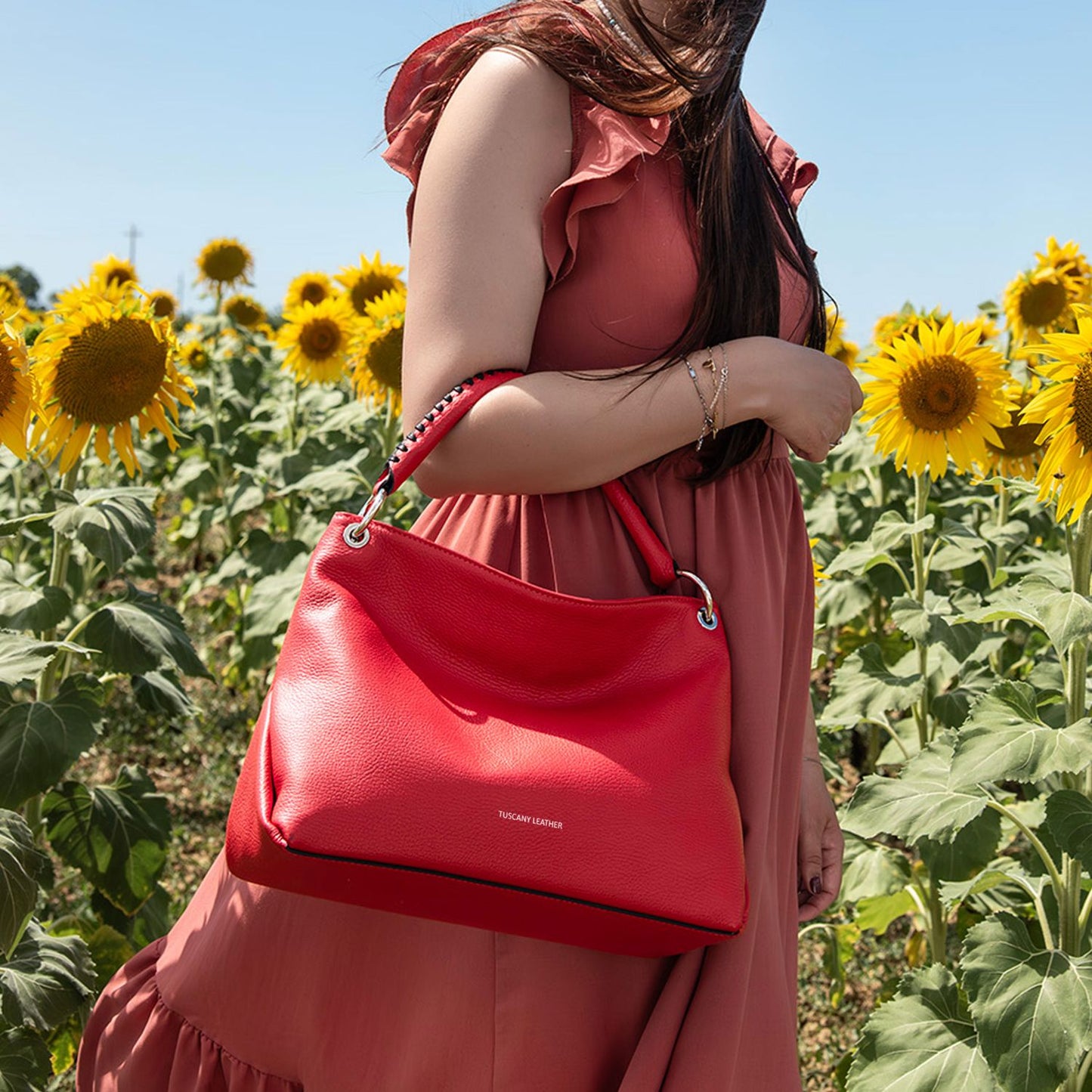 Red soft Italian leather shoulder bag with silver ring hardware carried by a woman in a sunflower field.
