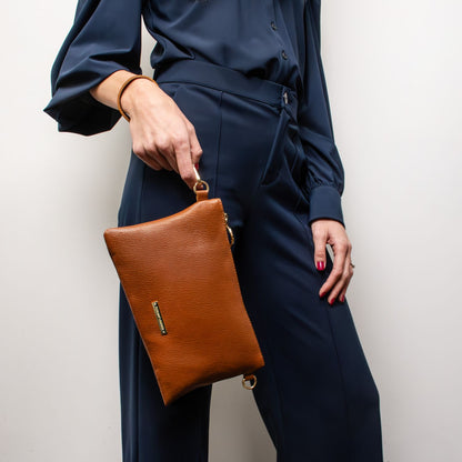 Tan pebbled leather pouch clutch held by a model wearing a navy blue tailored outfit.