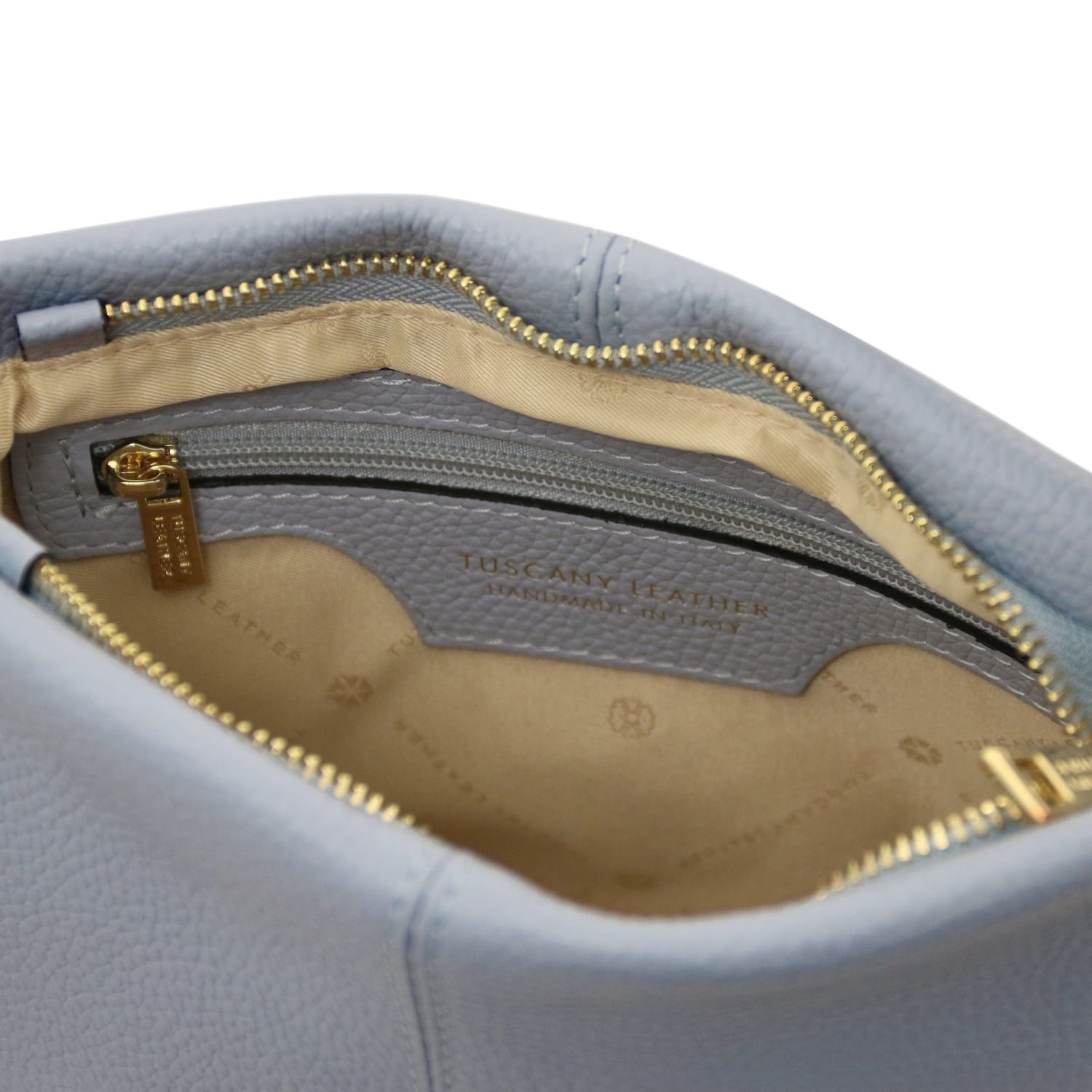 Close-up of light blue soft leather shoulder bag interior showing beige fabric lining, zippered pocket, and gold-tone zipper pull.