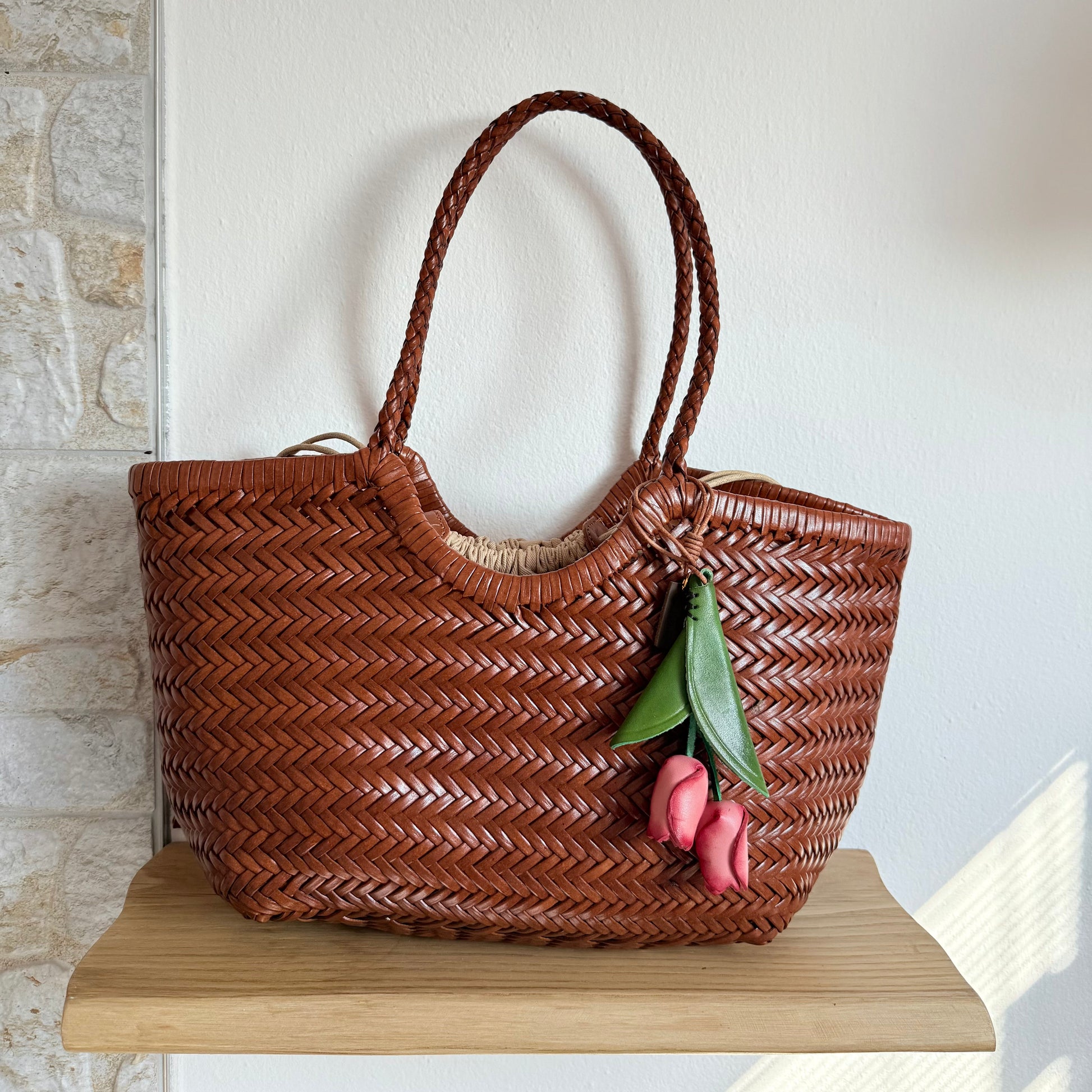 Brown woven handbag with a decorative flower on a wooden surface