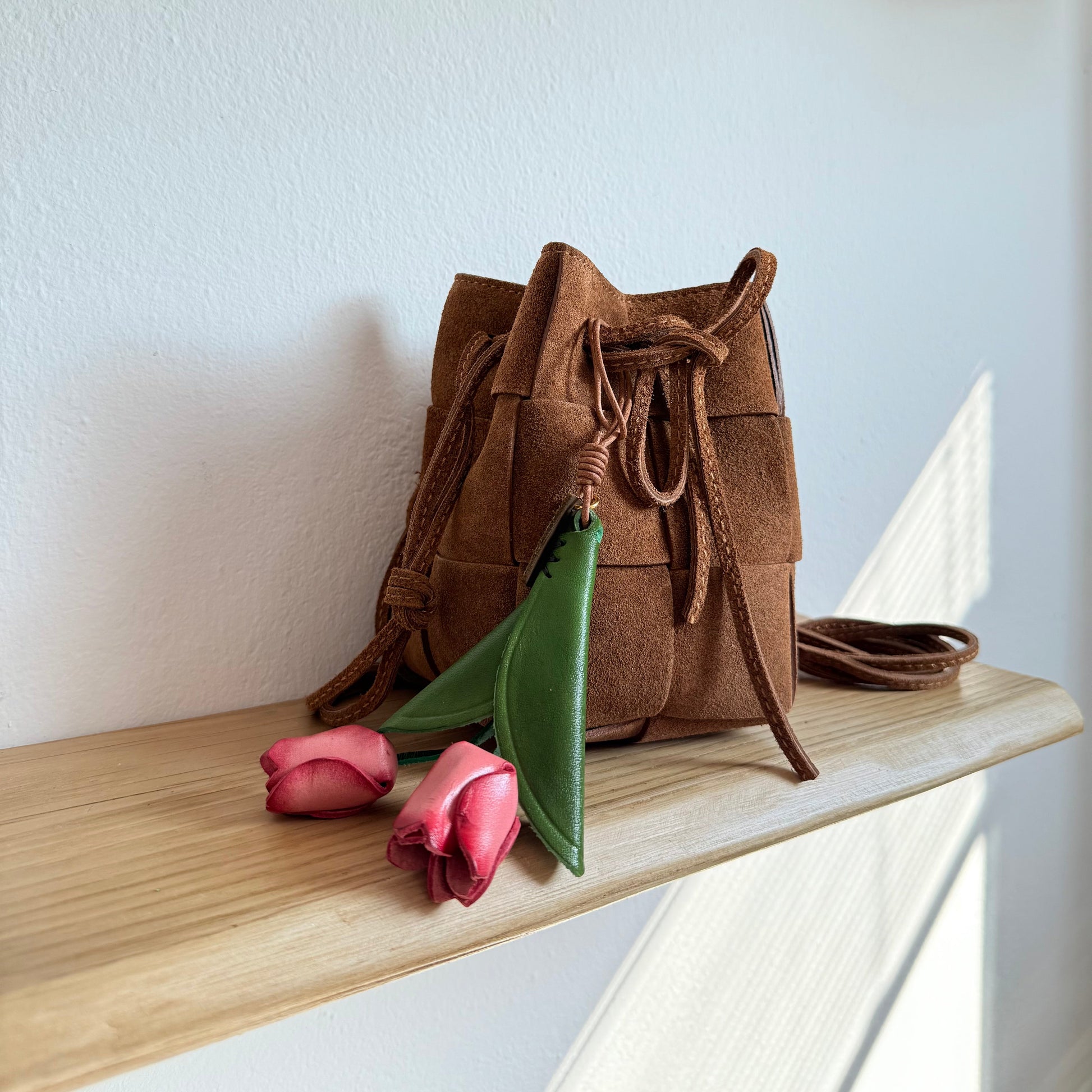 Tulip Bag Charm - Handmade Full-Grain Leather with pink petals and green leaves hanging from brown woven leather bag on wooden shelf.