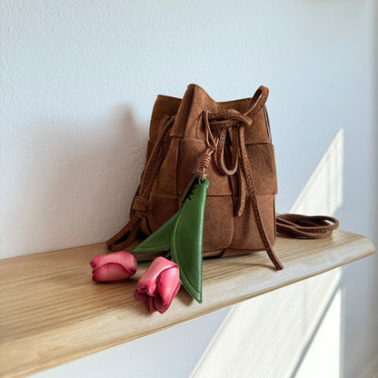 Tulip Bag Charm - Handmade Full-Grain Leather with pink petals and green leaves hanging from brown woven leather bag on wooden shelf.