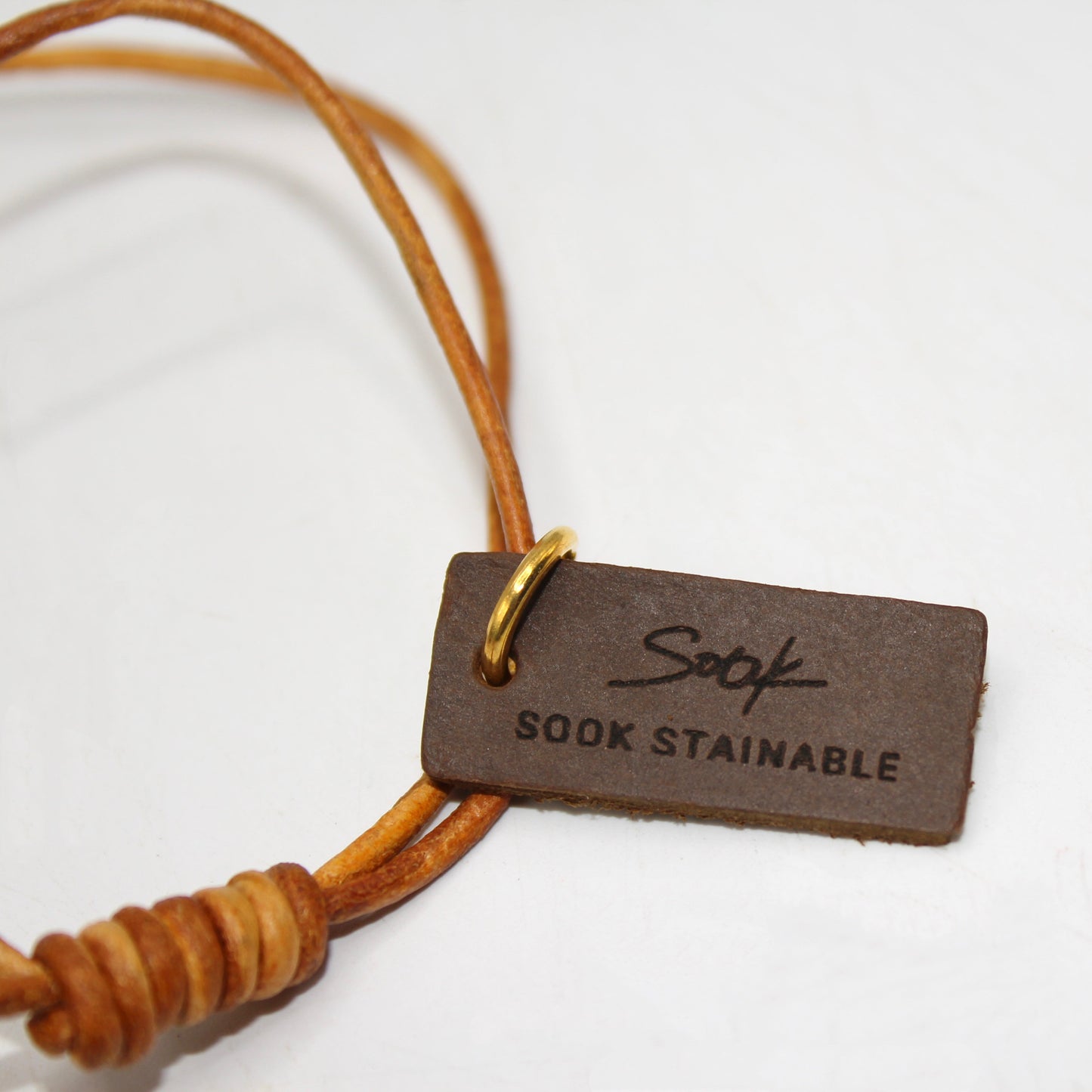 Leather tag on tan cord featuring SOOK Stainable branding with gold ring attachment on white background for Tulip Bag Charm - Handmade Full-Grain Leather.