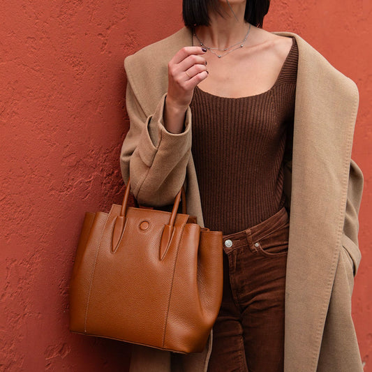 Person holding a brown Tulipan leather handbag against a red wall
