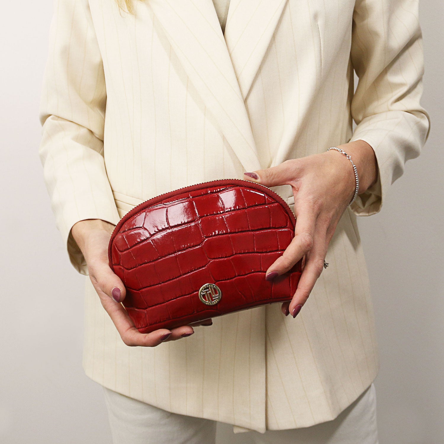 Vera - Croc print leather toiletry case | TL142514 in deep red with embossed leather, ferragens douradas, and zip closure held by person in cream blazer.