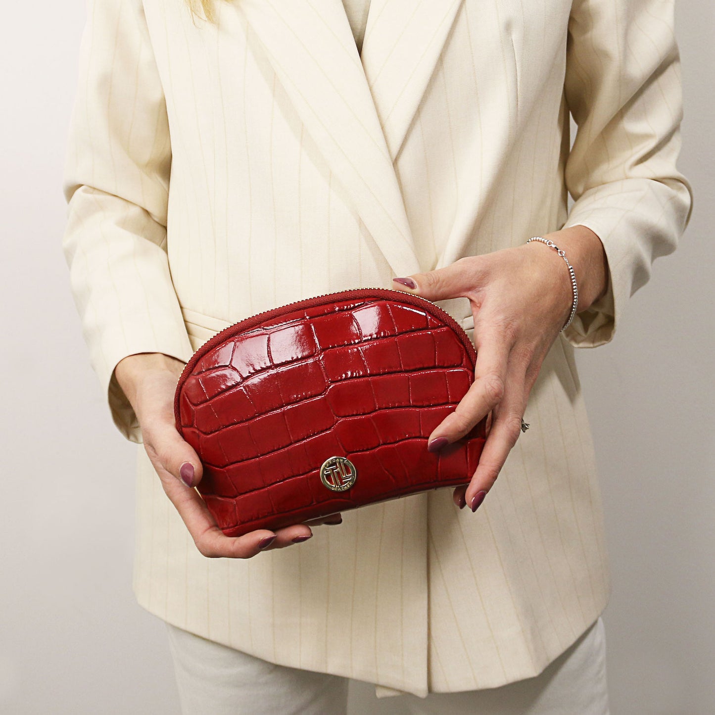 Vera - Croc print leather toiletry case | TL142514 in red embossed leather with ferragens douradas and zip closure held against a cream blazer