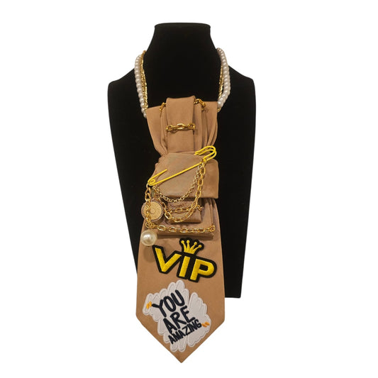 Beige You Are Amazing 4-in-1 Jeweled Tie adorned with gold chains and patches on a display bust